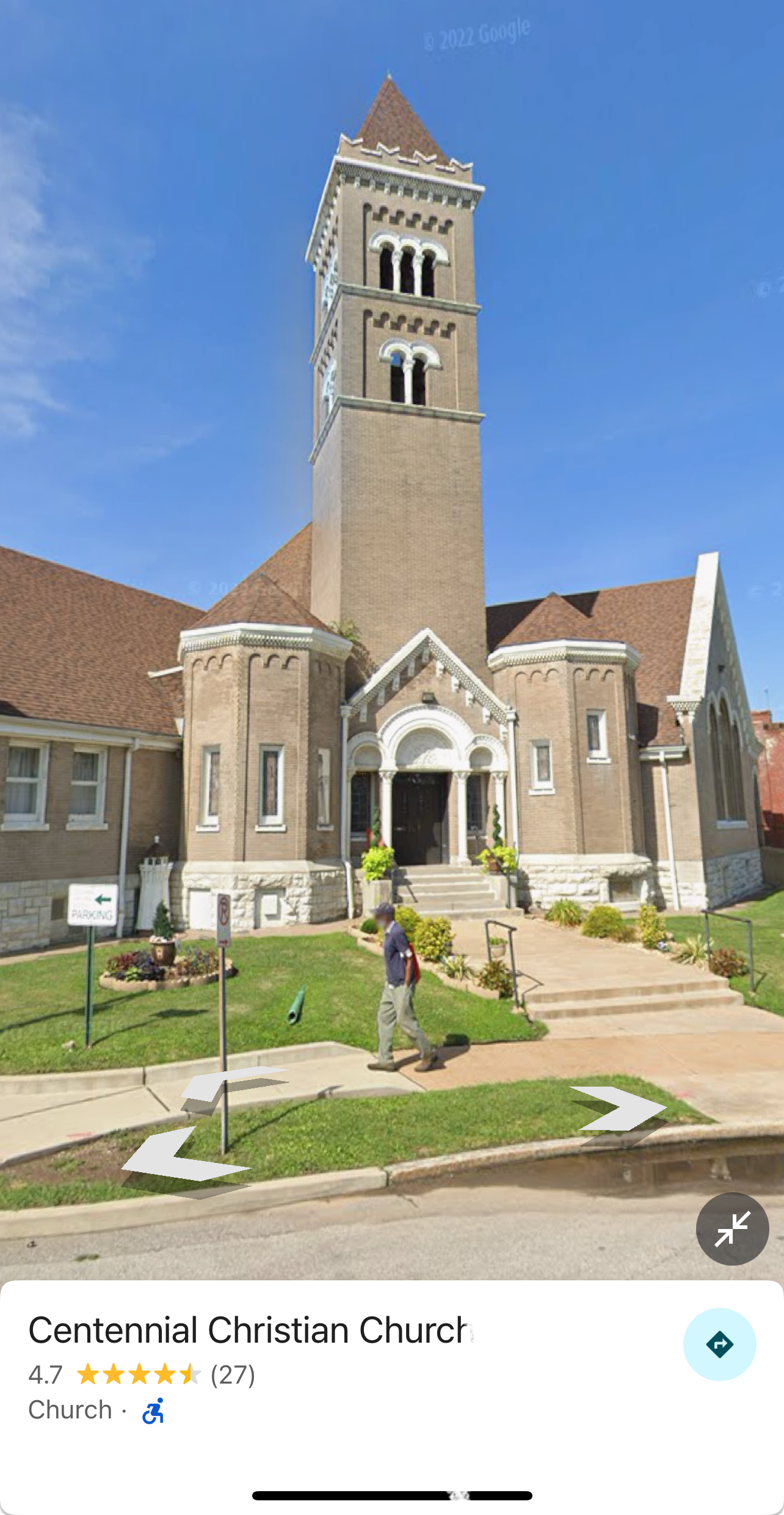 A person walks past the historical Centennial Christian Church, characterized by its tall bell tower and brick facade.